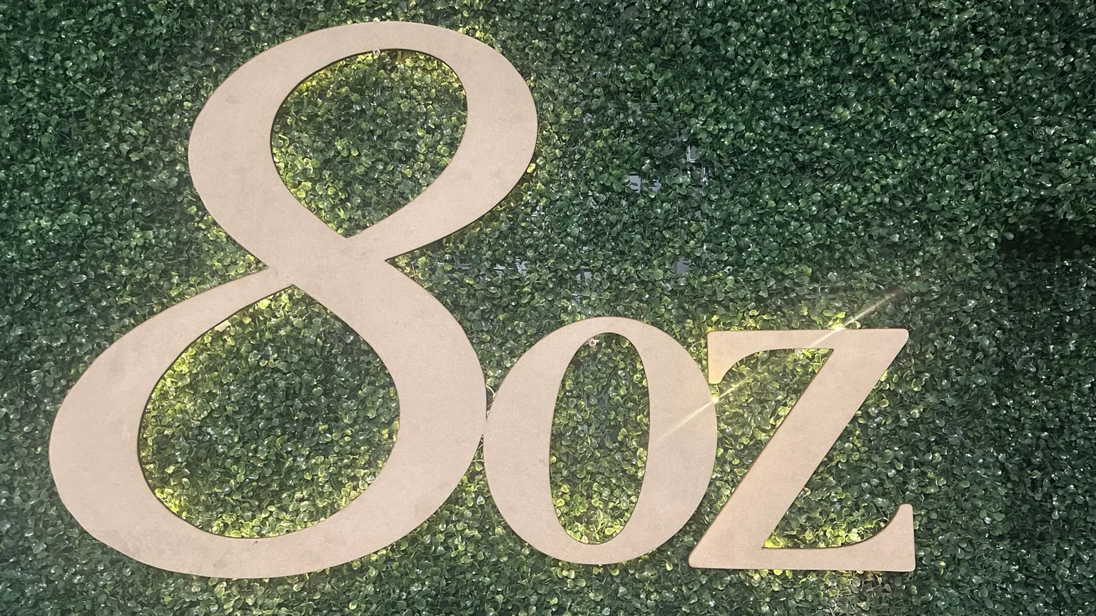 Logo de 8oz Café sobre pared vegetal